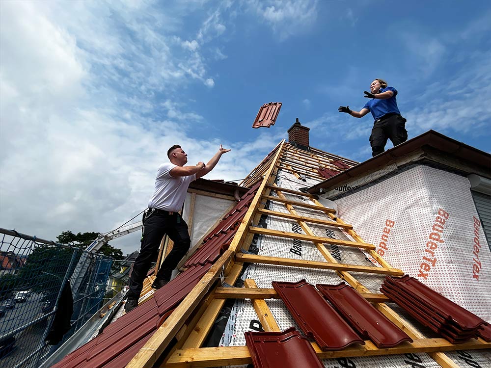 Dachdecker Christian Vogel wirft seiner Auszubildenden einen Dachziegel zu