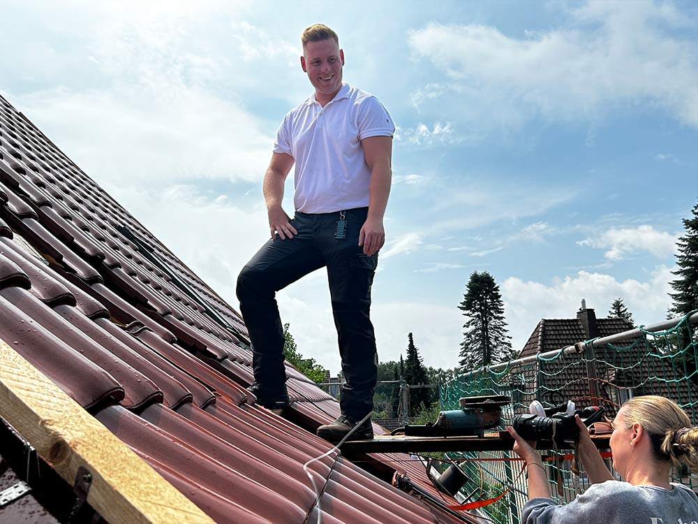 Dachdecker Christian Vogel steht auf dem Dach und neben ihm die Fotografin